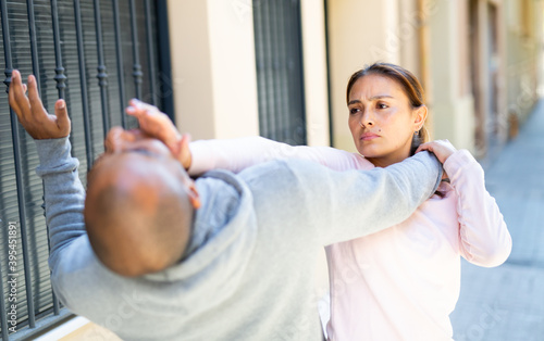 Quadro em tela Determined young Latina using Krav Maga techniques to protect herself from attacker man on city street