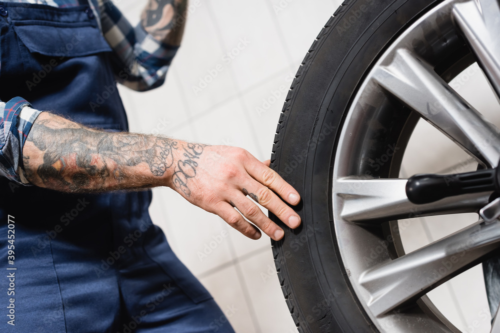 partial of tattooed technician touching car wheel in workshop on blurred background partial of tattooed technician touching car wheel in workshop on blurred background