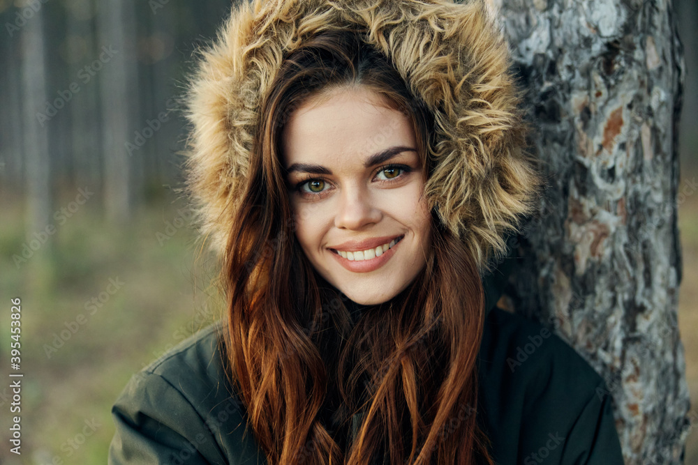 Woman in a jacket with a hood near a tree on a forest background cropped view Woman in a jacket with a hood near a tree on a forest background cropped view