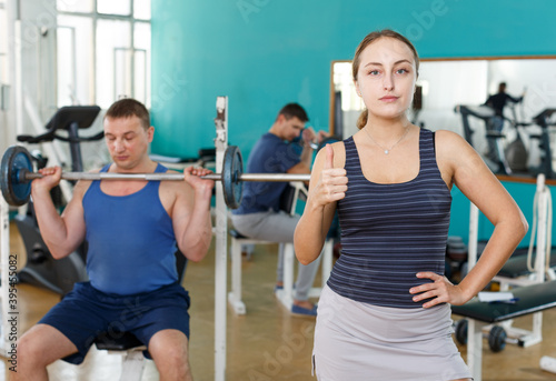 Portrait of positive sporty girl on background of exercising men in gym