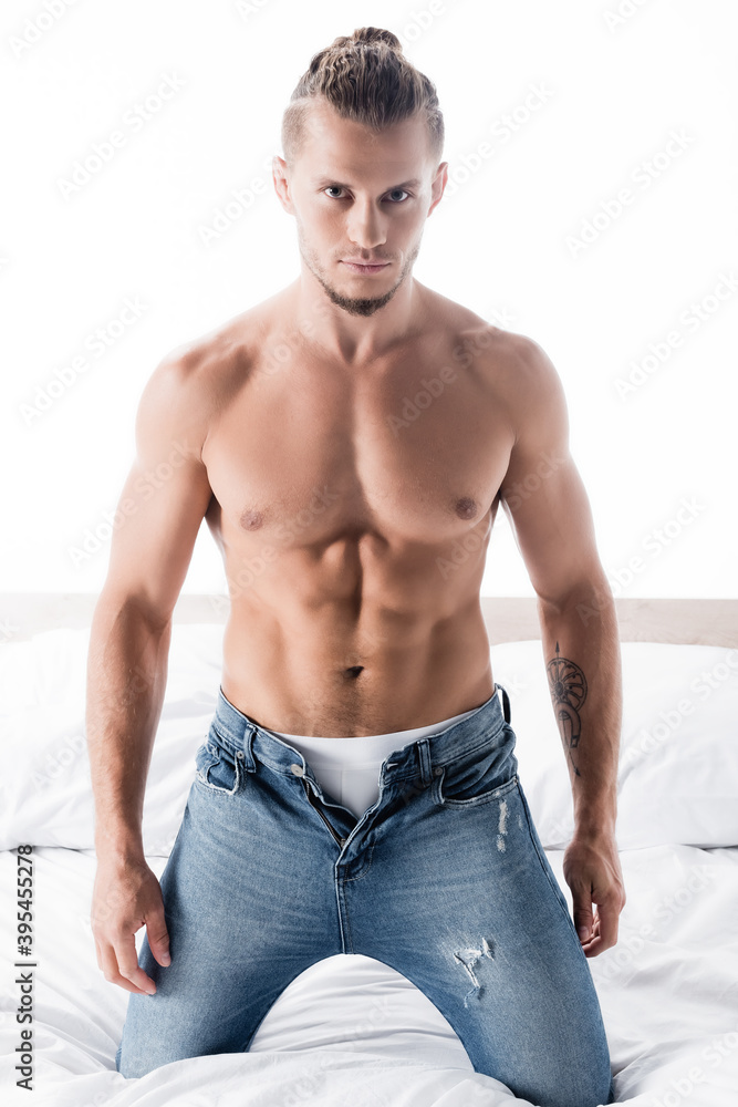 Obraz premium shirtless man in jeans posing in bed isolated on white