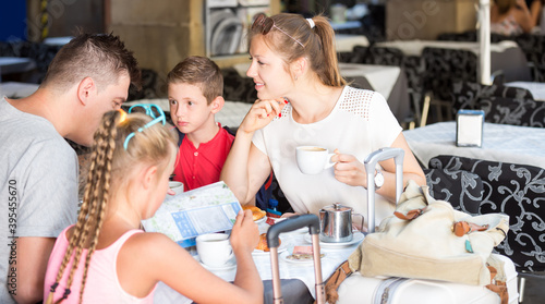 Fotografie Glad parents with two kids relaxing in cafe searching location on map