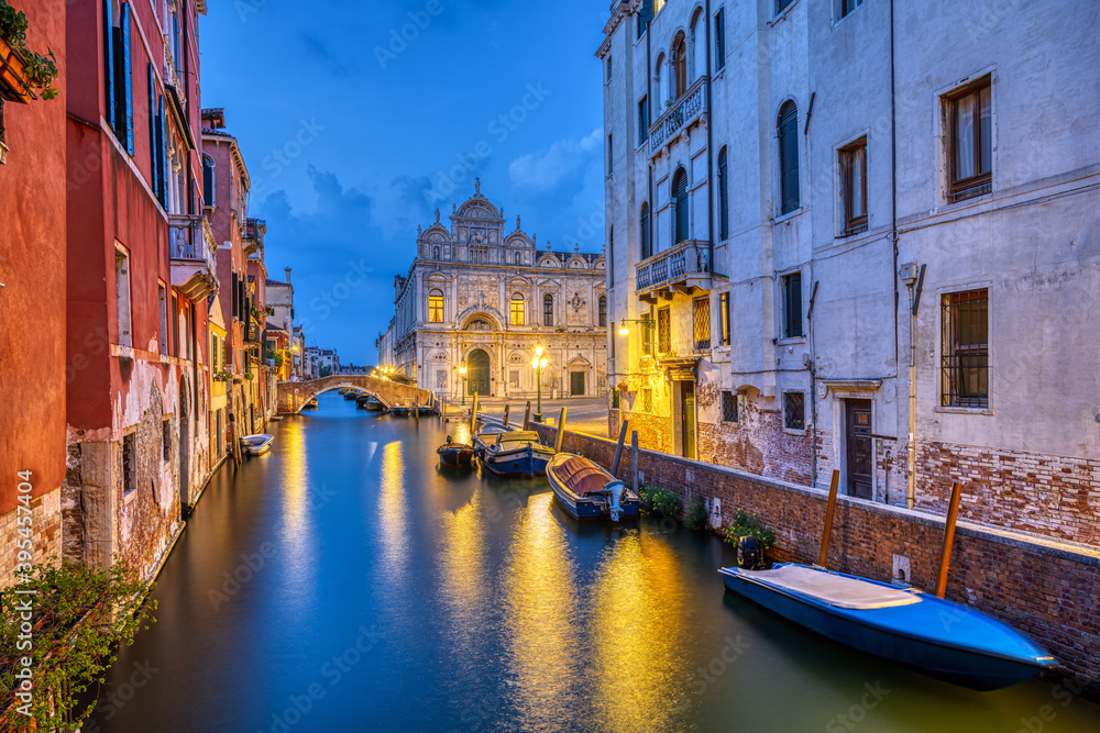 Canal in the old town of Venice at dusk with the Scuola Grande di San Marco in the back
