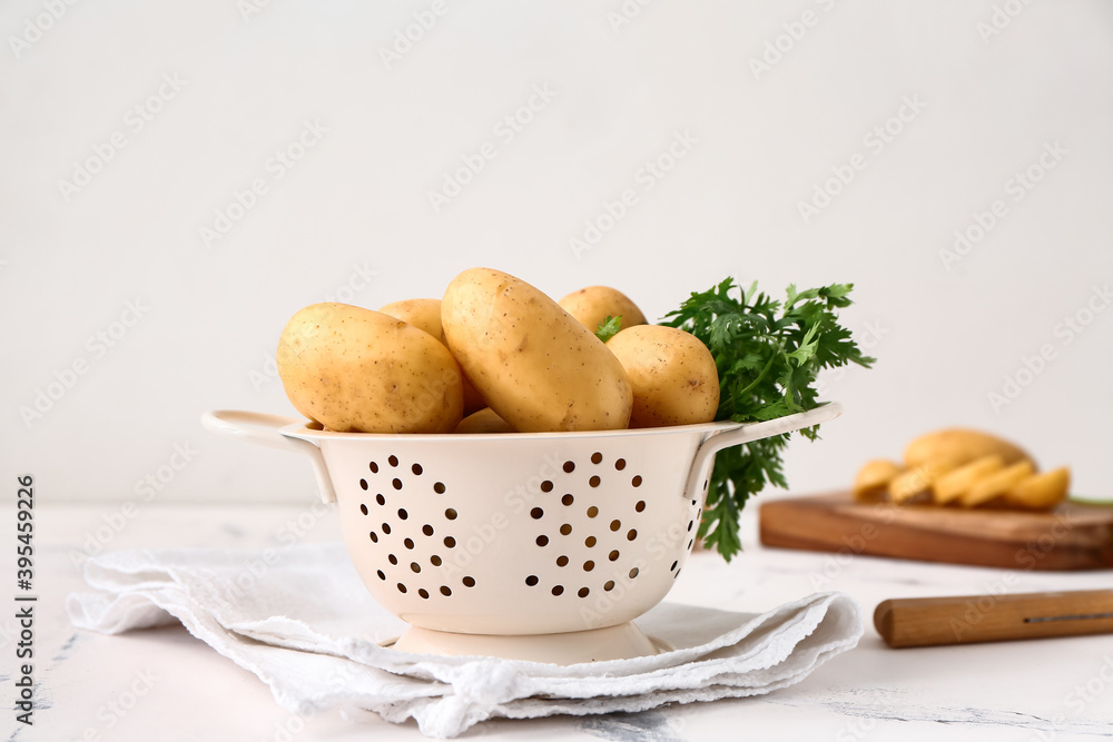 Colander with raw potatoes on light background