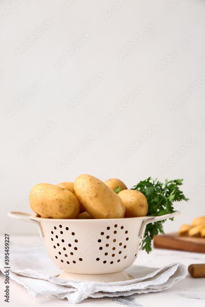Colander with raw potatoes on light background Colander with raw potatoes on light background