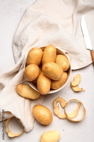 Bowl with raw potatoes on light background