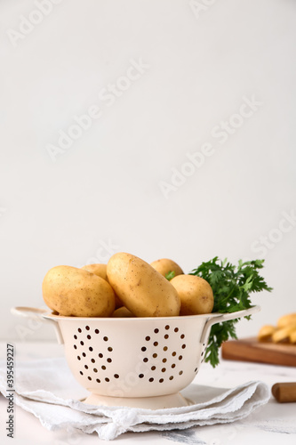 Colander with raw potatoes on light background