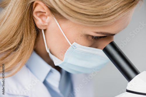 close up of scientist in medical mask looking through microscope, stock image