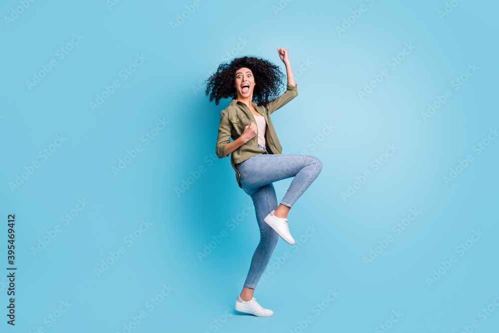 Full size profile portrait of delighted lady fists up open mouth raise knee celebrate isolated on blue color background