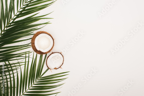 Top view of coconut halves near palm leaves on white background with copy space  stock image