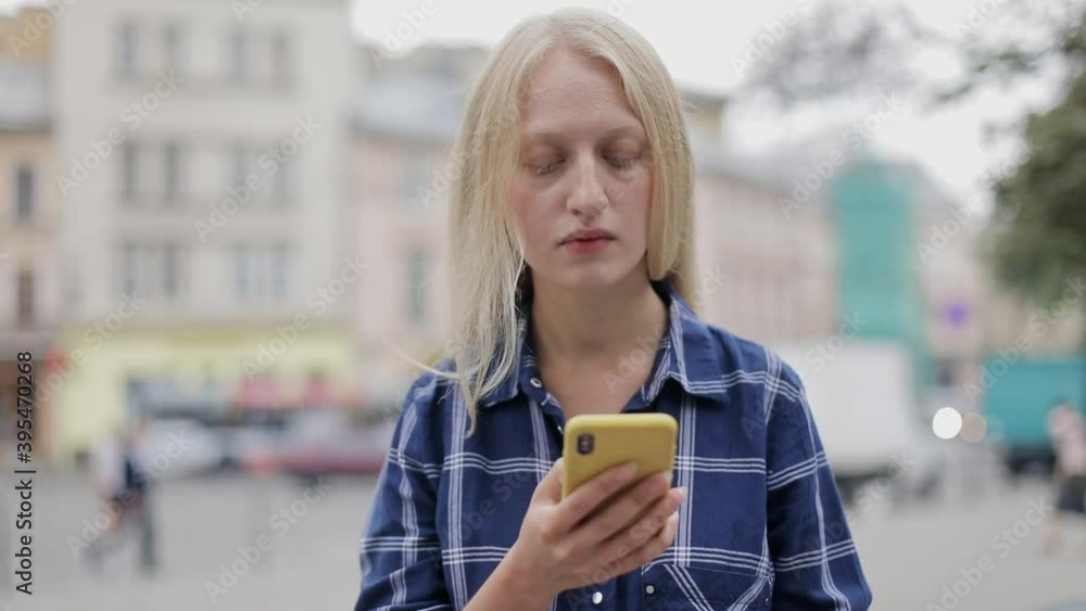 Crop view of young woman with blond hair holding and using smartphone. Portrait of female person browsing internet while standing at city street. Concept of communication. Crop view of young woman with blond hair holding and using smartphone. Portrait of female person browsing internet while standing at city street. Concept of communication.