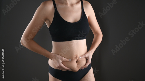 The young woman shows changes in her figure. Concept of body care, proper nutrition, excess weight, women's health. Woman in underwear on grey background.  © Tatsiana