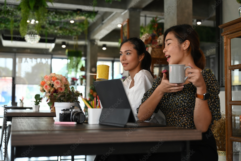 A two young female freelancer are sharing ideas while drinking coffee together in modern office.