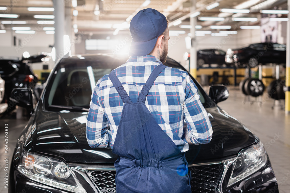 back of mechanic in overalls and cap standing in workshop near cars back of mechanic in overalls and cap standing in workshop near cars