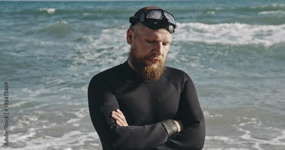 Portrait of man with beard on background of sea waves. Adult serious man swimmer looking into the frame. Young single man in diver's suit in beautiful place. Portrait of man with beard on background of sea waves. Adult serious man swimmer looking into the frame. Young single man in diver's suit in beautiful place.