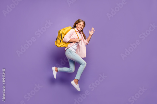 Full size profile photo of optimistic pretty girl jump wave hand wear pink shirt jeans sneakers rucksack isolated on violet background
