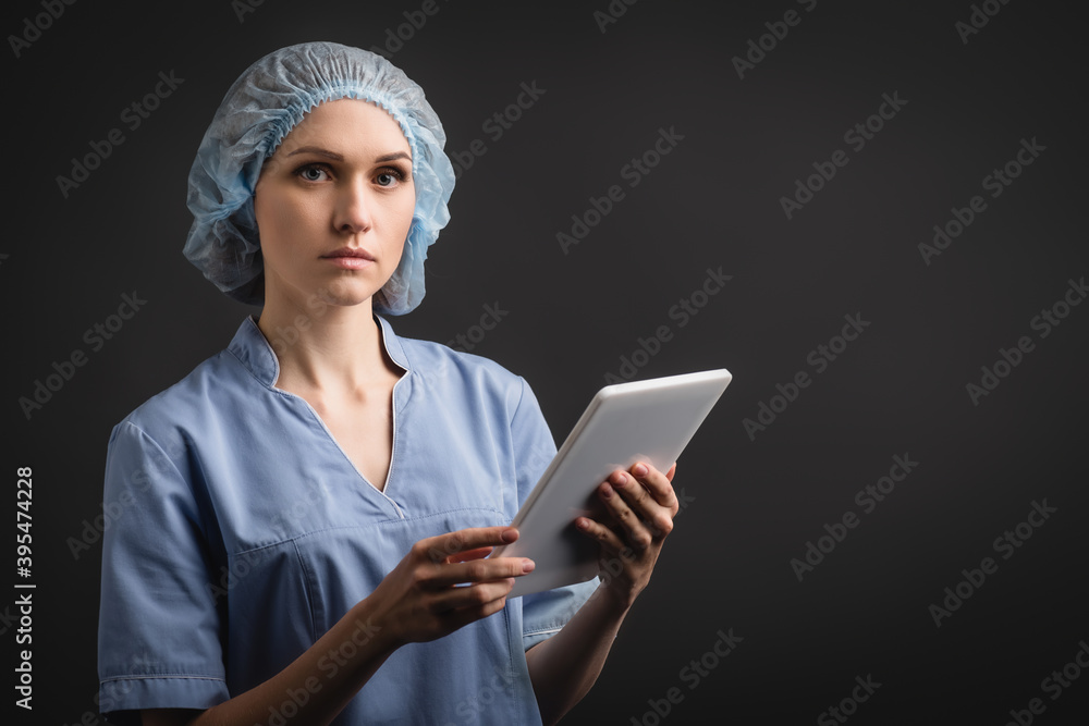 nurse in medical cap and uniform holding digital tablet isolated on dark nurse in medical cap and uniform holding digital tablet isolated on dark