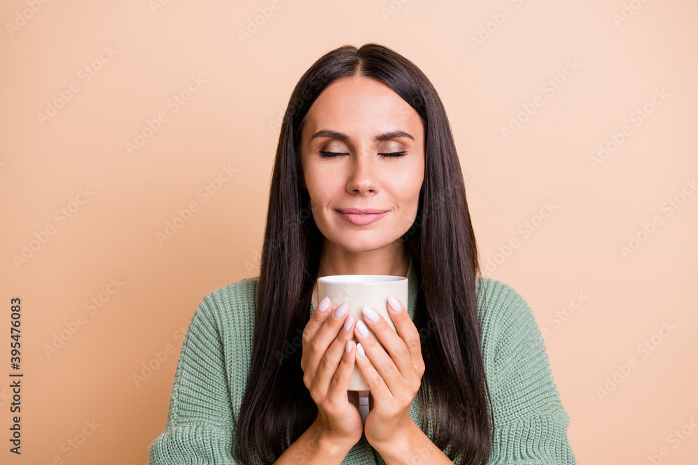 Portrait of optimistic girl smell cup closed eyes wear green sweater isolated on peach color background Portrait of optimistic girl smell cup closed eyes wear green sweater isolated on peach color background