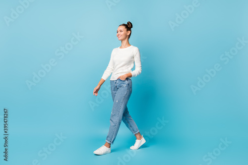 Photo of dreamy girl walk hand pocket wear white sweater jeans footwear isolated blue color background