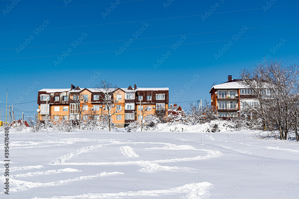 Multi-storey residential buildings made of white and red brick with plastic Windows, stand in winter under a layer of white lush snow in frosty Sunny weather.