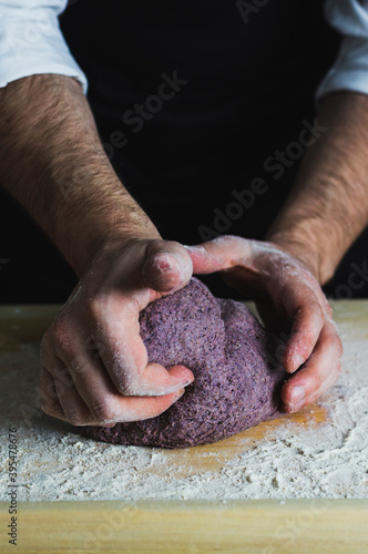 A man kneading a purple bread dough on a floured wooden surface