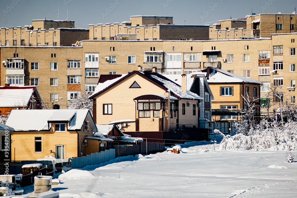 Obraz premium Multi-storey residential buildings made of white and red brick with plastic Windows, stand in winter under a layer of white lush snow in frosty Sunny weather.