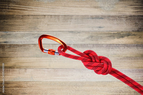 Carabiner D-Shaped in orange colorn Tied to red rope equipment on wooden background. photo