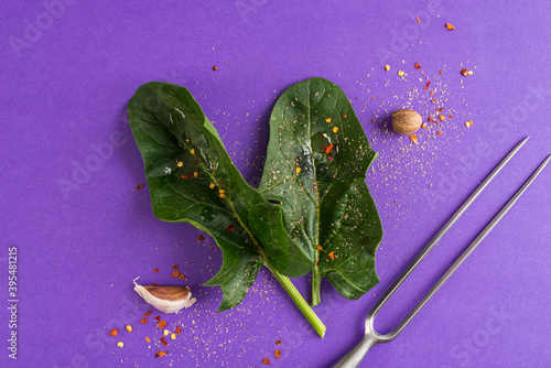Fresh spinach, spices and a meat fork on a violet surface