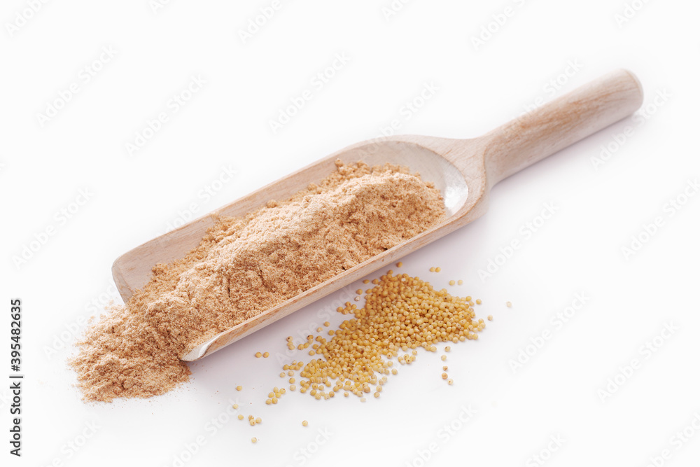 Brown millet flour on a wooden scoop, with millet next to it Brown millet flour on a wooden scoop, with millet next to it