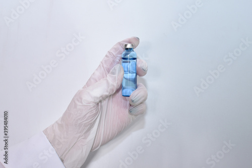 A hand in a medical glove holds an ampoule with a vaccine against the coronavirus infection COVID-19 on a white background. Vaccine. Ampoule with medicine. Doctor holds an injection drug in his hand.