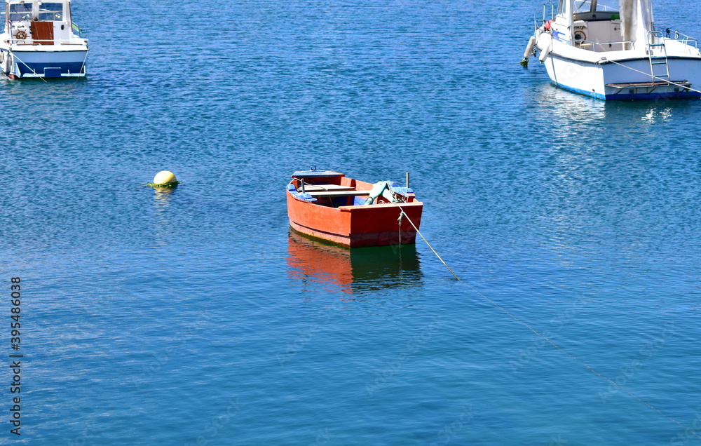 Red wooden rowboat floating on the sea moored in a harbor. Rias Baixas, Galicia, Spain.