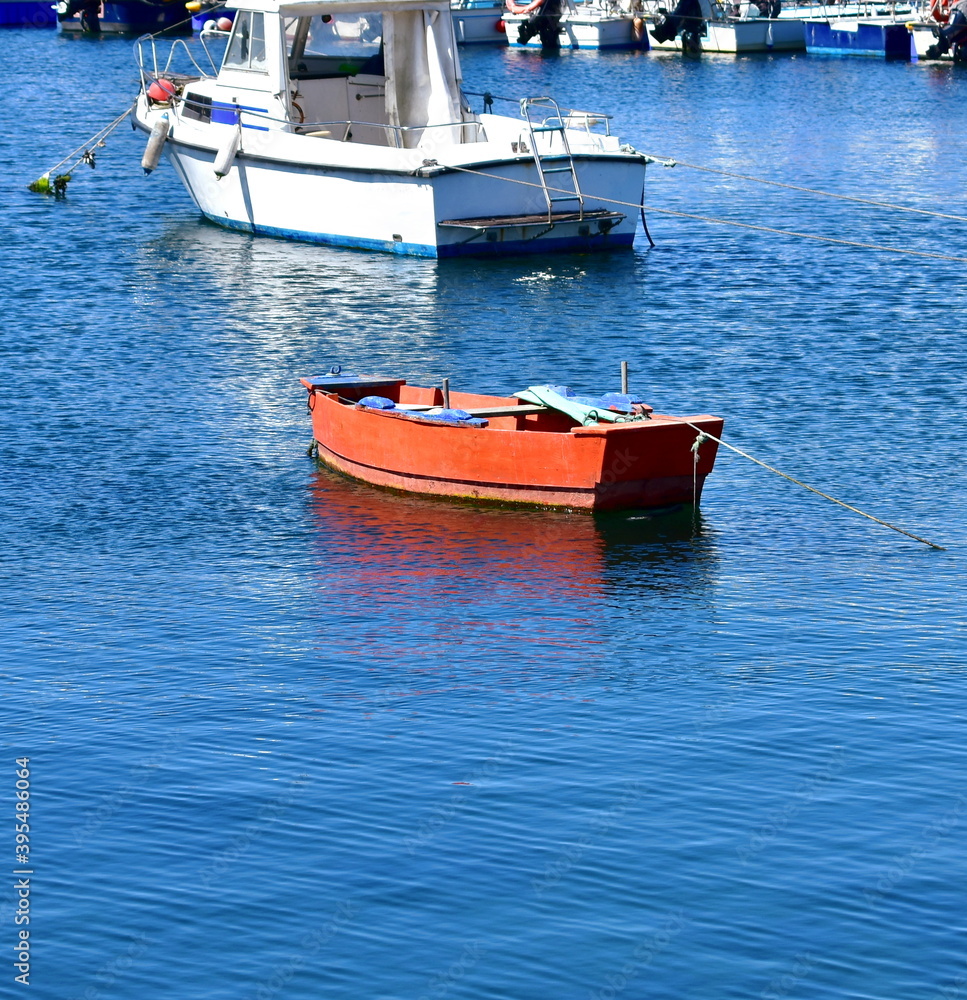 Red wooden rowboat floating on the sea moored in a harbor. Rias Baixas, Galicia, Spain.