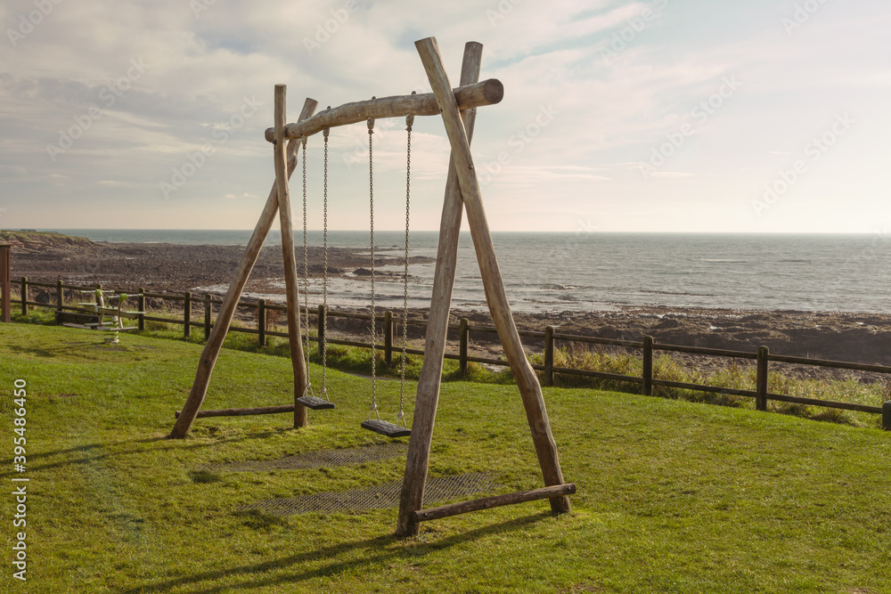Fototapeta premium Two children's swings in a park by the seaside, at Crail, Fife, Scotland. The swings are empty, ready for the next two children to have some fun.