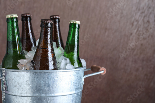 Metal bucket with bottles of beer and ice cubes on brown background, closeup. Space for text