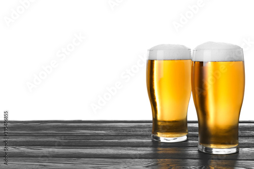 Glasses of tasty beer on black wooden table against white background
