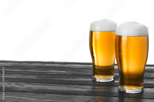 Glasses of tasty beer on black wooden table against white background. Space for text