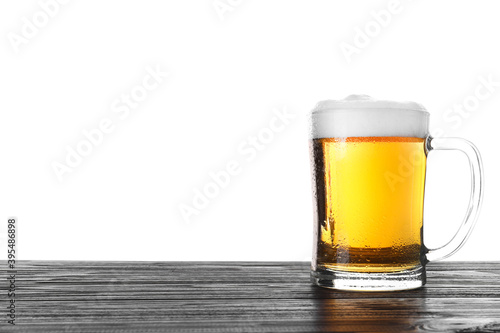 Glass mug with tasty beer on black wooden table against white background