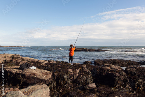 A 6yr old boy is fishing in the sea at Crail, Fife, Scotland. His tackle box and a bag are on the rocks behind him. He is using a weedless lure. photo
