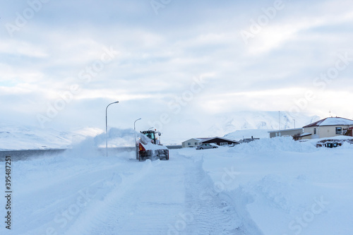 The tractor cleans snow on the road after a heavy snowfall. A snow blower removes snow from the road in the morning. Winter landscape of a small town in Iceland.