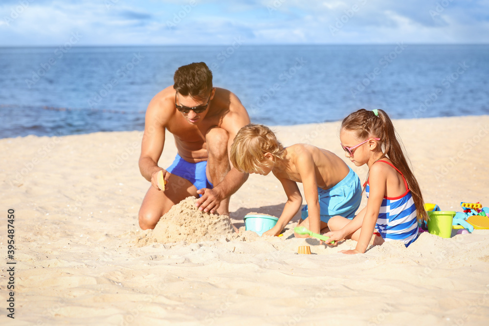 Father and children playing on sandy beach near sea. Summer holidays with family Father and children playing on sandy beach near sea. Summer holidays with family