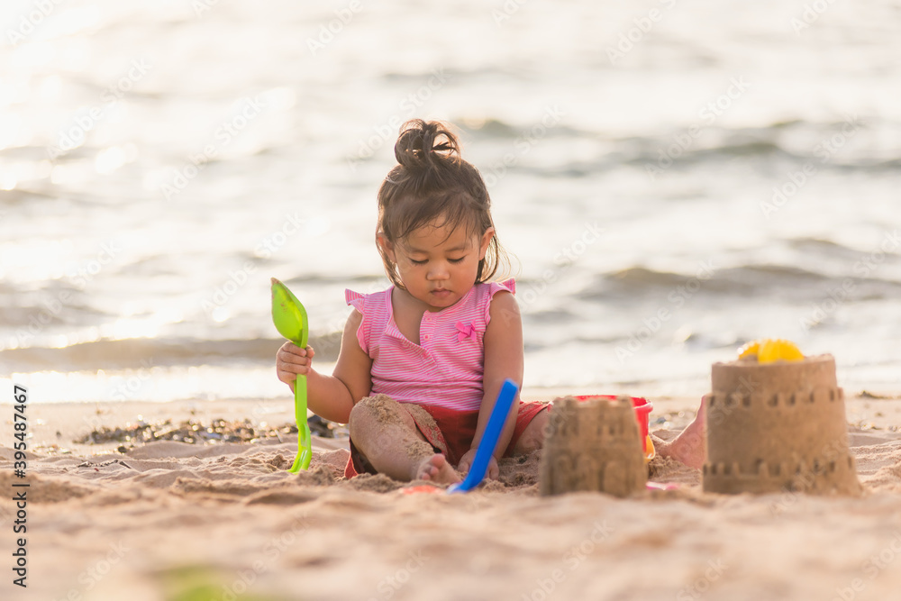 Happy fun Asian child cute little girl playing sand with toy sand tools at a tropical sea beach in holiday summer on sunset time, tourist trip concept Happy fun Asian child cute little girl playing sand with toy sand tools at a tropical sea beach in holiday summer on sunset time, tourist trip concept