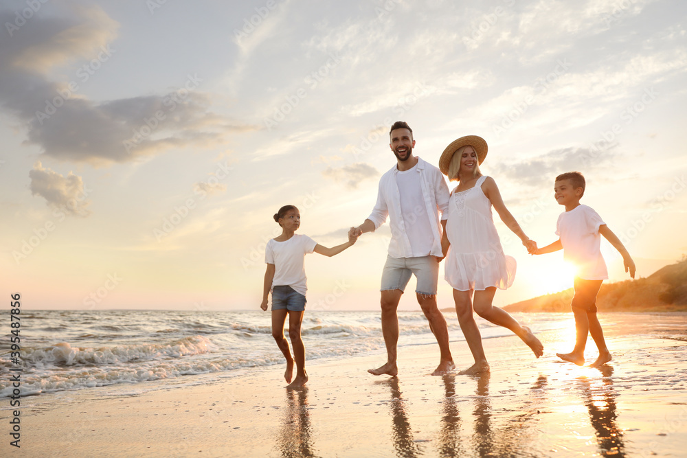 Happy family running on sandy beach near sea at sunset