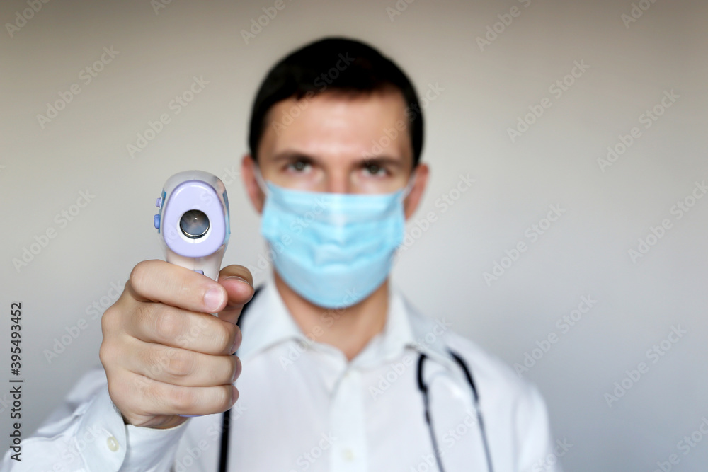 Man in medical mask measures body temperature, coronavirus symptoms. Doctor with digital isometric non-contact thermometer in his hand, safety measures during covid-19 quarantine Man in medical mask measures body temperature, coronavirus symptoms. Doctor with digital isometric non-contact thermometer in his hand, safety measures during covid-19 quarantine