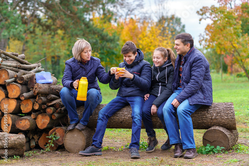 family relaxing outdoor in autumn city park  happy people together  parents and children  they drink tea  talking and smiling  beautiful nature