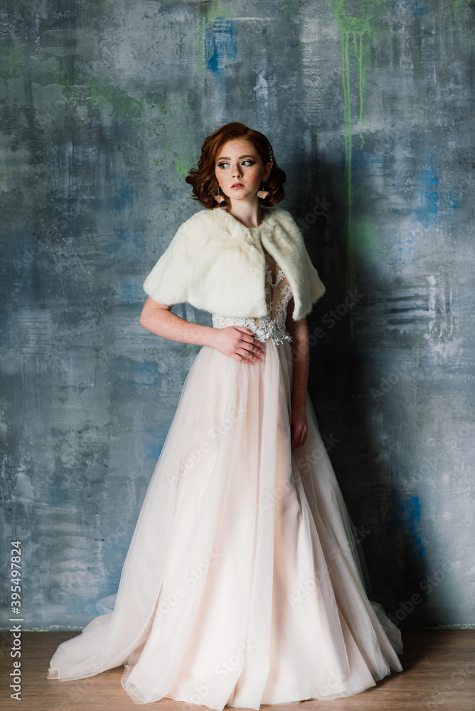 Portrait of red haired girl wearing wedding dress against a white studio background.