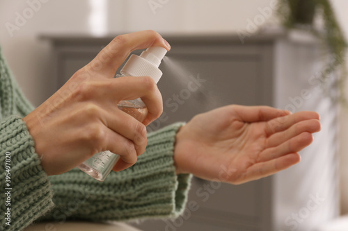 Young woman applying antiseptic spray indoors, closeup