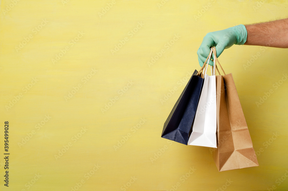 Man wearing protective gloves and holding three shoppin bags against bright yellow background.Empty space.Concept of prevention treatments against covid-19
