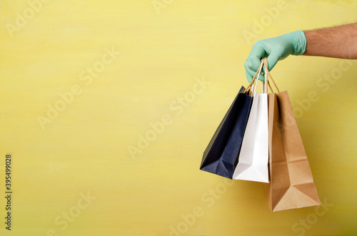 Man wearing protective gloves and holding three shoppin bags against bright yellow background.Empty space.Concept of prevention treatments against covid-19