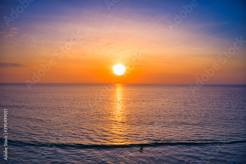 Aerial drone view Beautiful sunset over the clam sea with cloud and sky background. Sunset over tropical beach. Nature summer  concept. Peak sunset over sea with yellow light reflect in cloud.