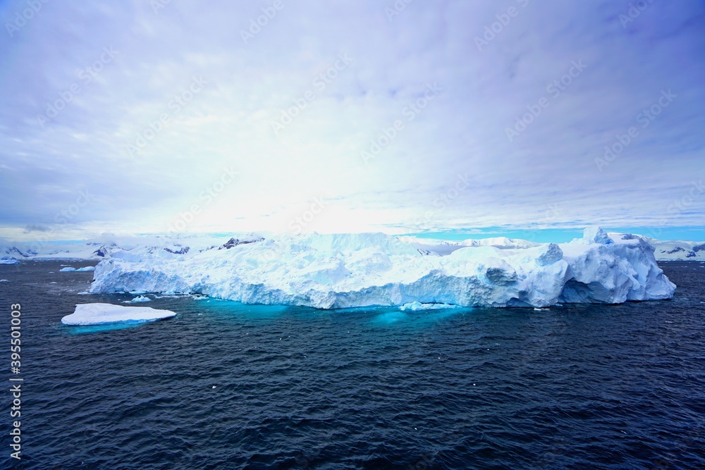Summer landscape in Antarctica with melting snow, sea, icebergs, white clouds.
